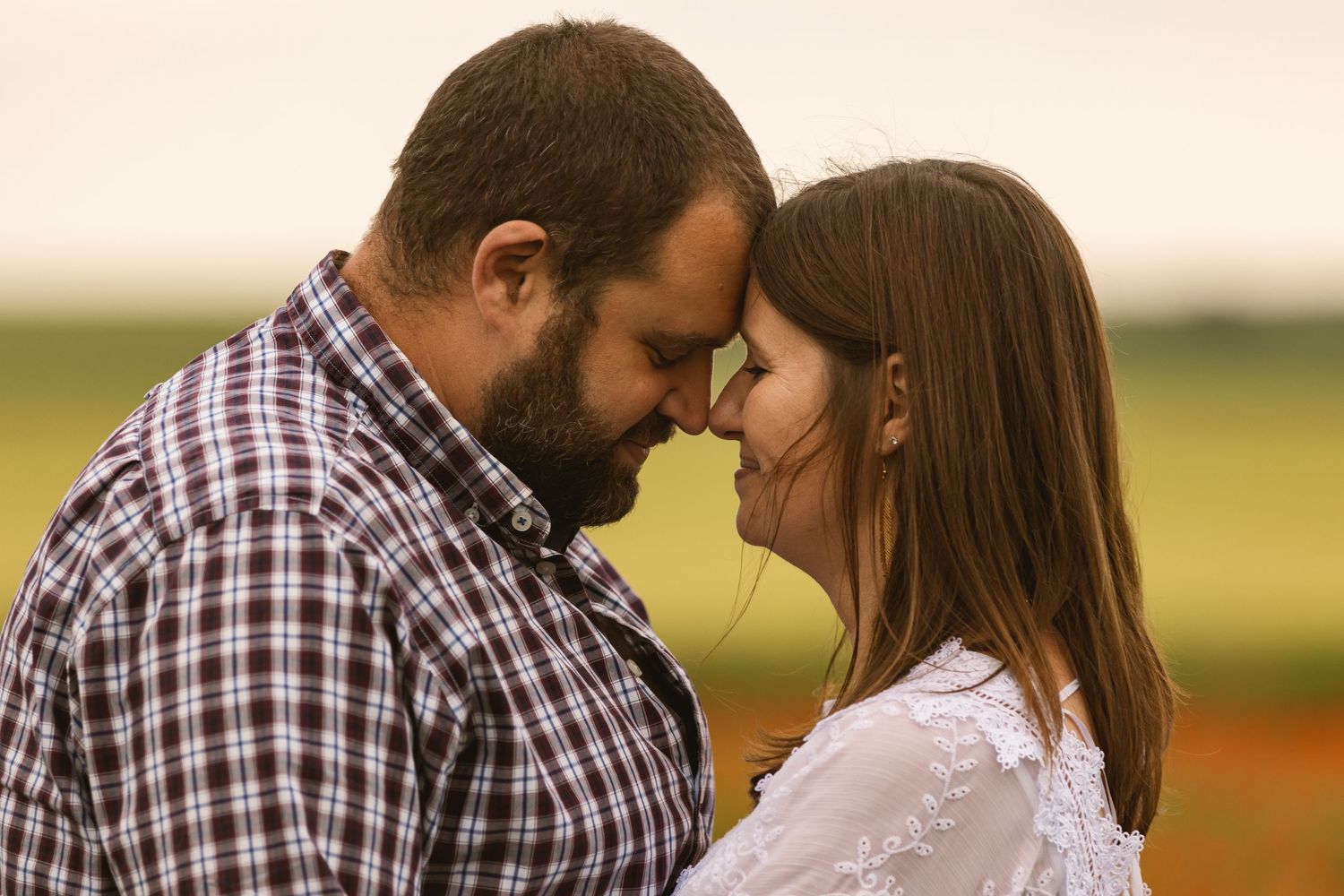 Romantic couple touching foreheads in a tender moment outdoors in a green field at sunset.