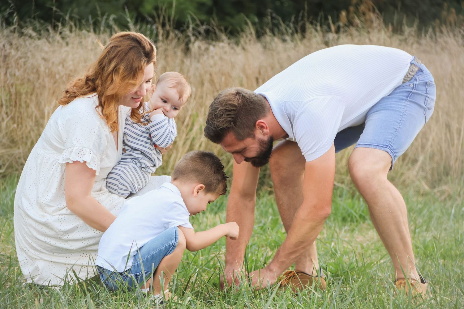 Séance famille lifestyle — jeune famille avec bébé et bambin jouant dans l'herbe près d'un champ de blé doré, photographe Aisne.