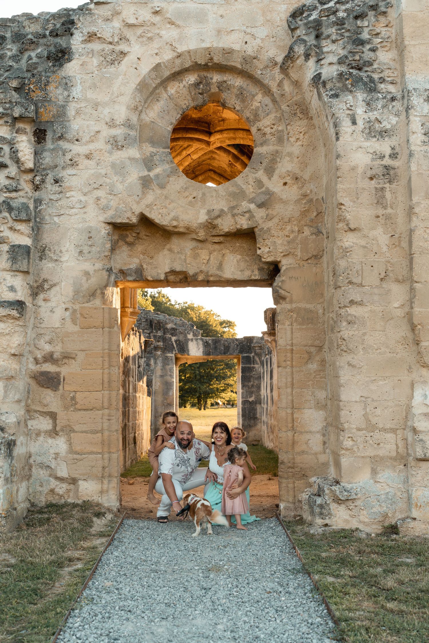 Family of four posing with a dog inside a historic stone archway at sunset in ancient ruins.