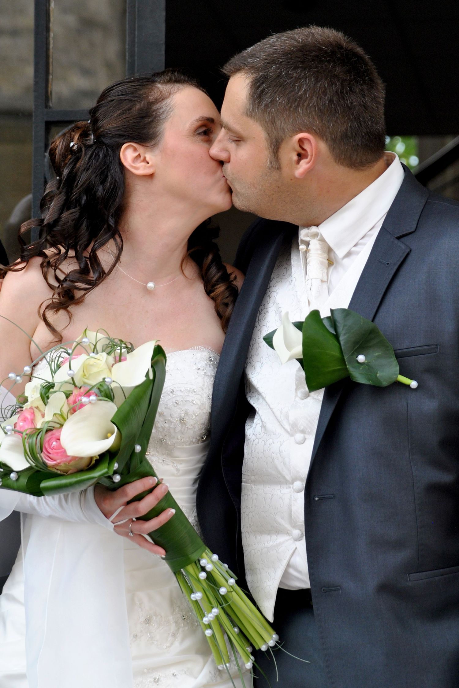 Newlywed couple sharing romantic kiss with bride holding pink and white bouquet.