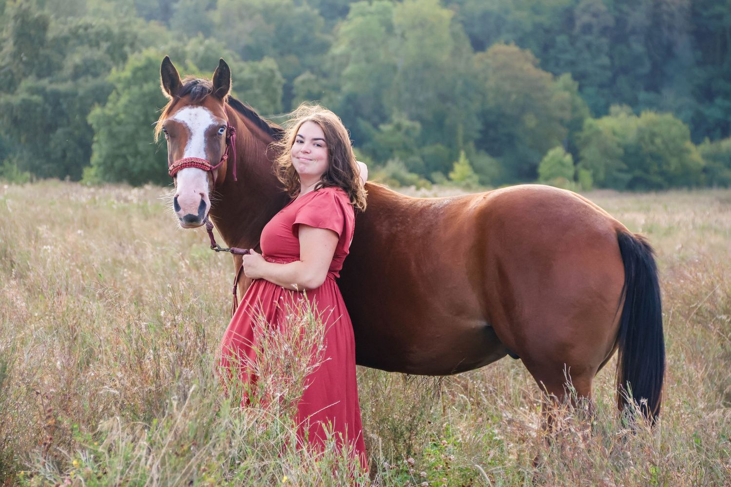 Séance cheval lifestyle — femme en robe rouge aux côtés de son cheval alezan dans une prairie dorée, photographe Soissons Aisne.