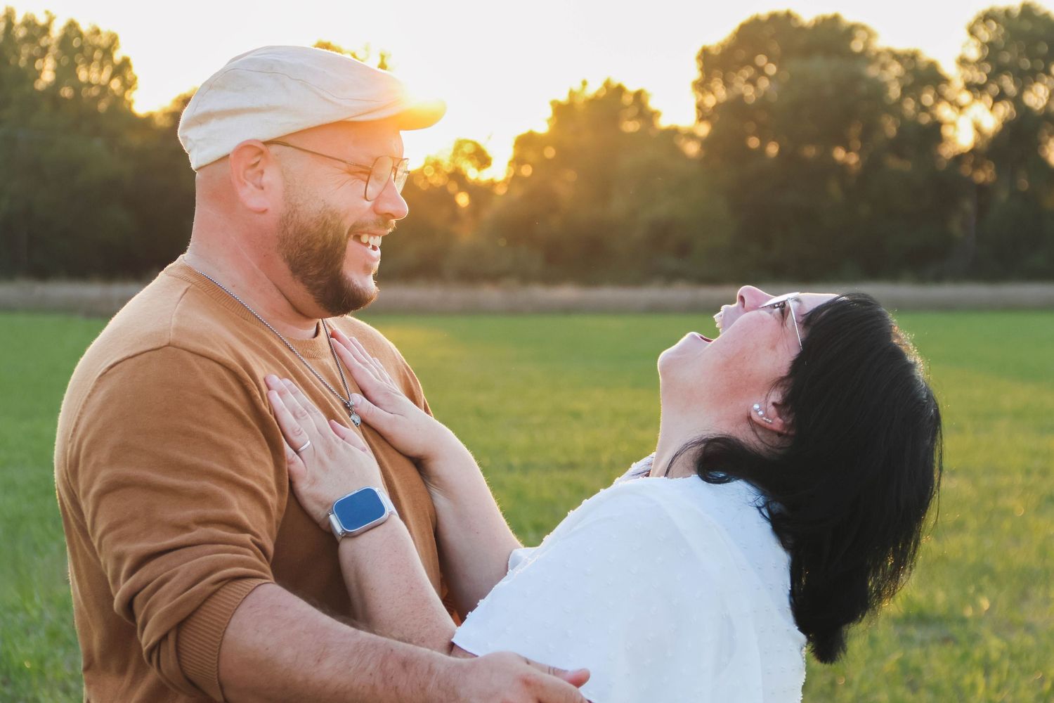 Séance couple lifestyle — couple souriant partageant un moment complice dans un champ verdoyant au coucher du soleil, photographe Soissons