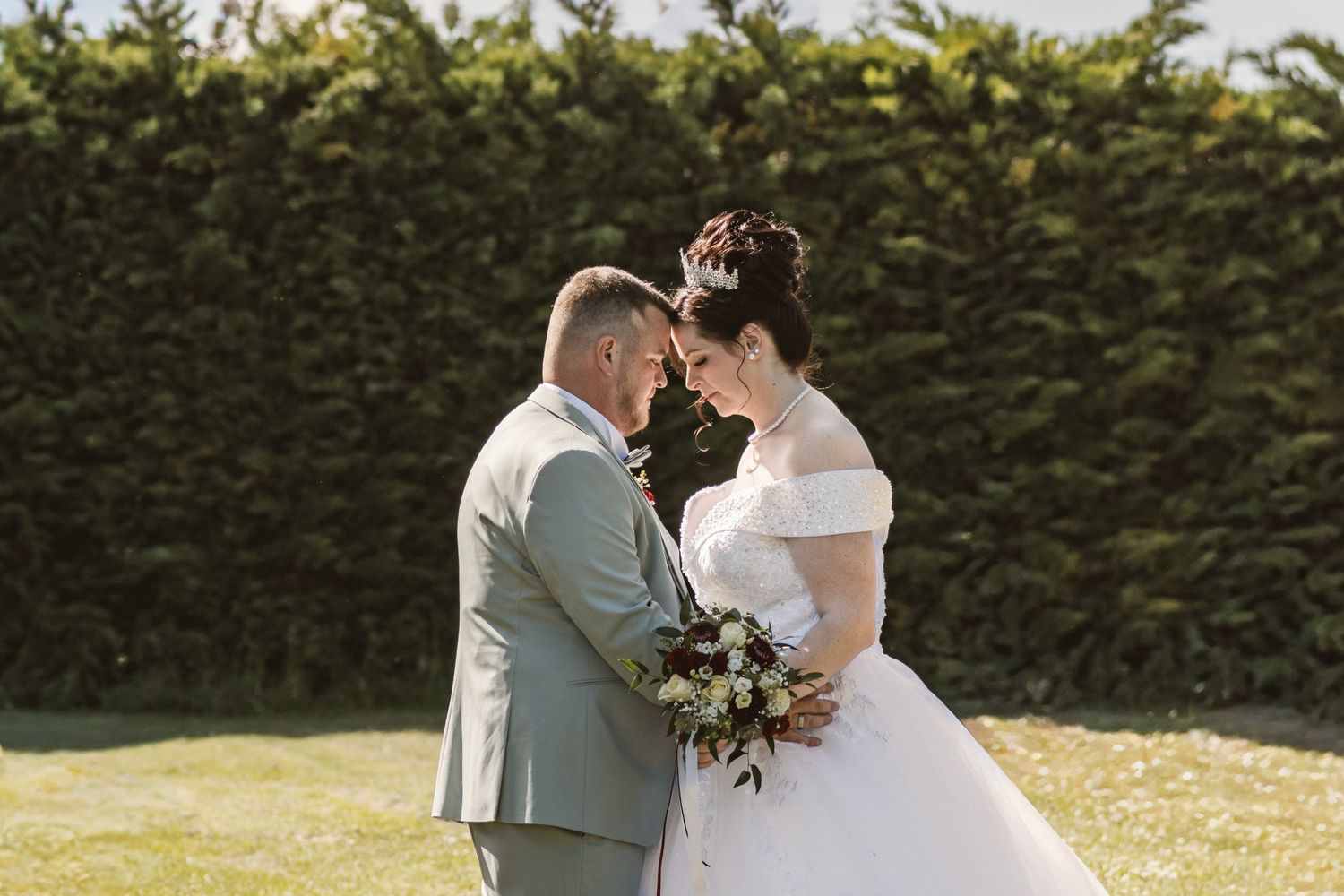 Bride and groom share a romantic moment in a garden, bride holding a bouquet in a white off-shoulder gown.