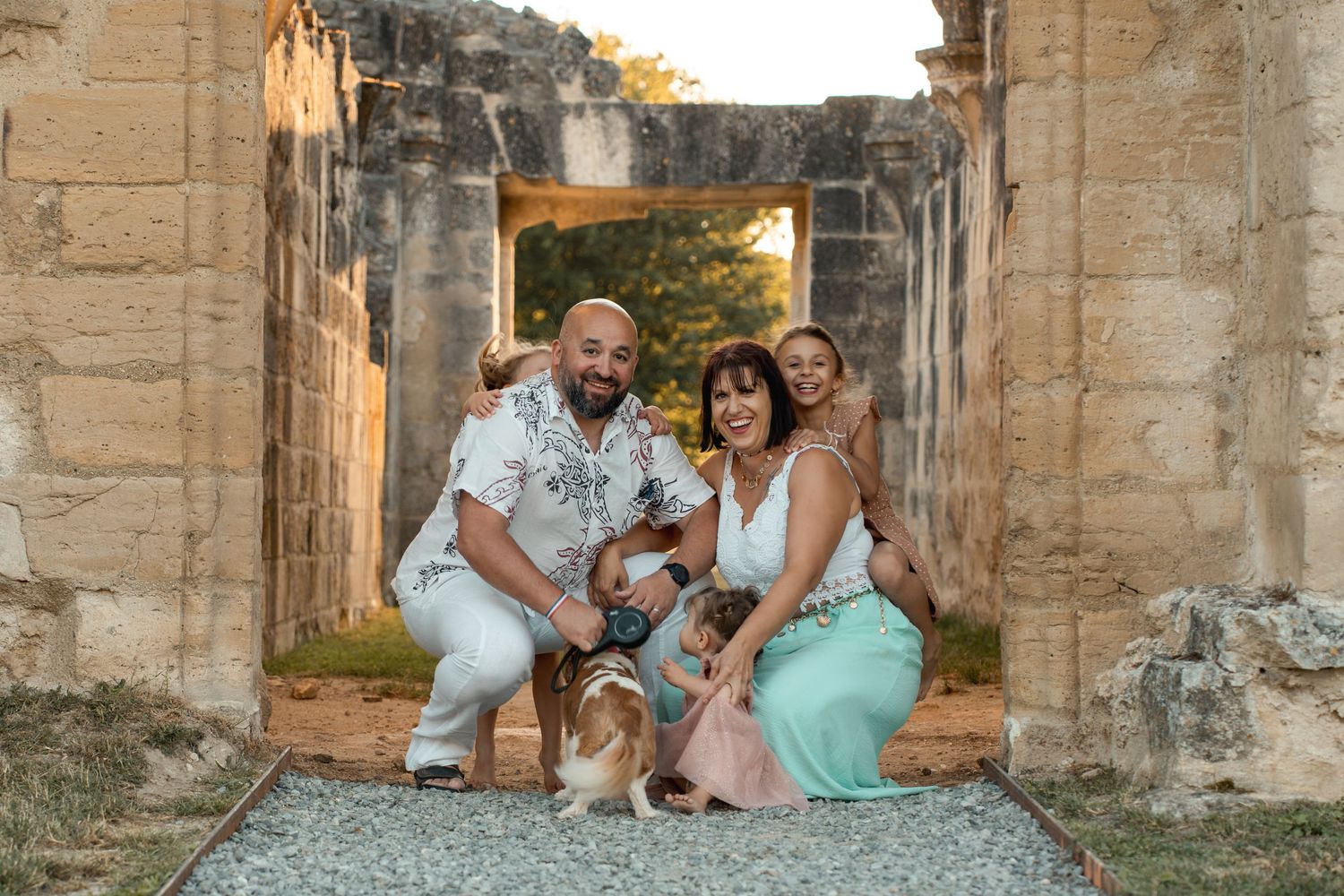 Happy family with dog poses inside historic stone ruins archway during a warm sunset.