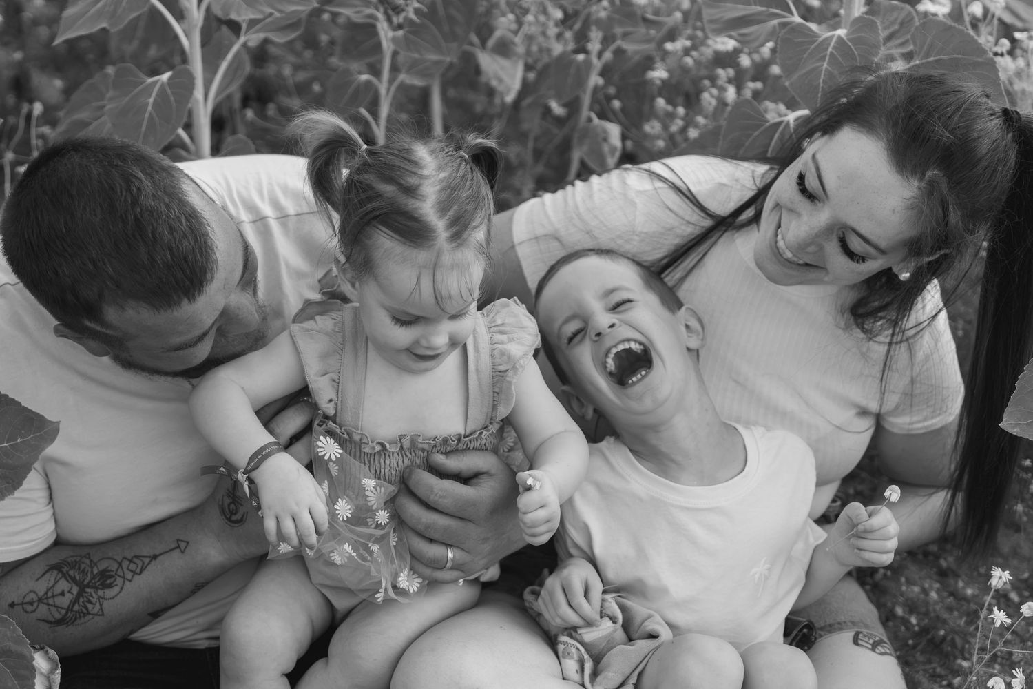 Black and white photo of a joyful family with two laughing children sitting outdoors together.