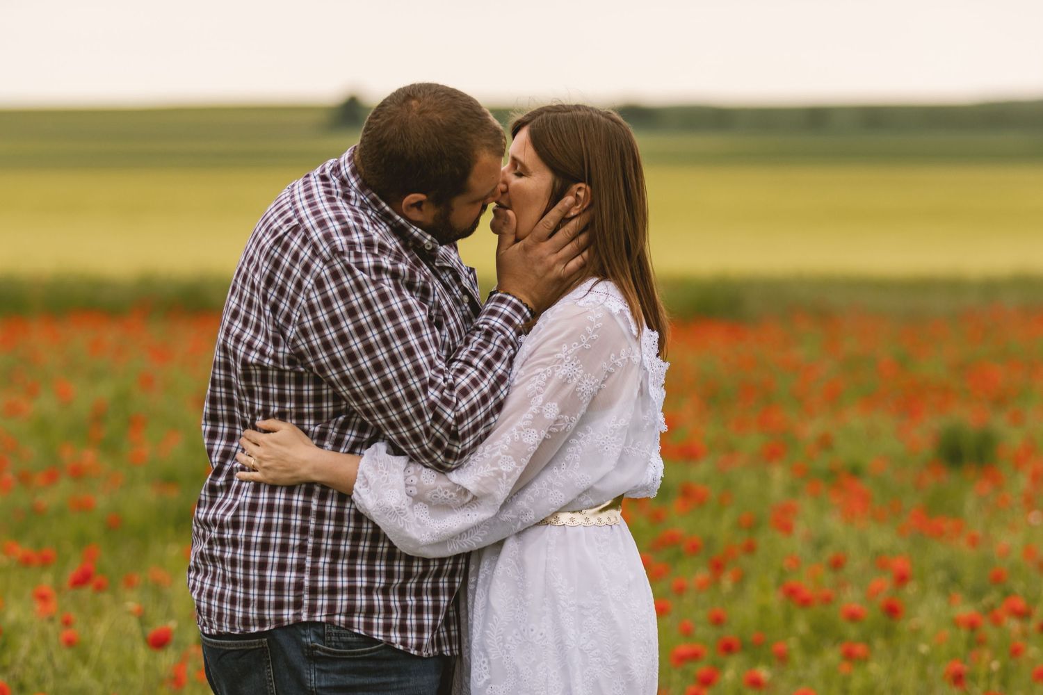 Couple sharing a tender kiss in a blooming red poppy field, embracing romantically in an outdoor setting.