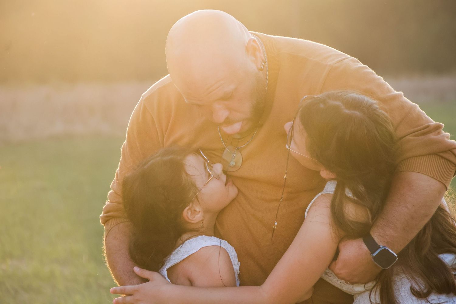 Séance famille lifestyle — papa enlaçant tendrement sa femme et son enfant dans la lumière dorée du coucher du soleil, photographe Reims