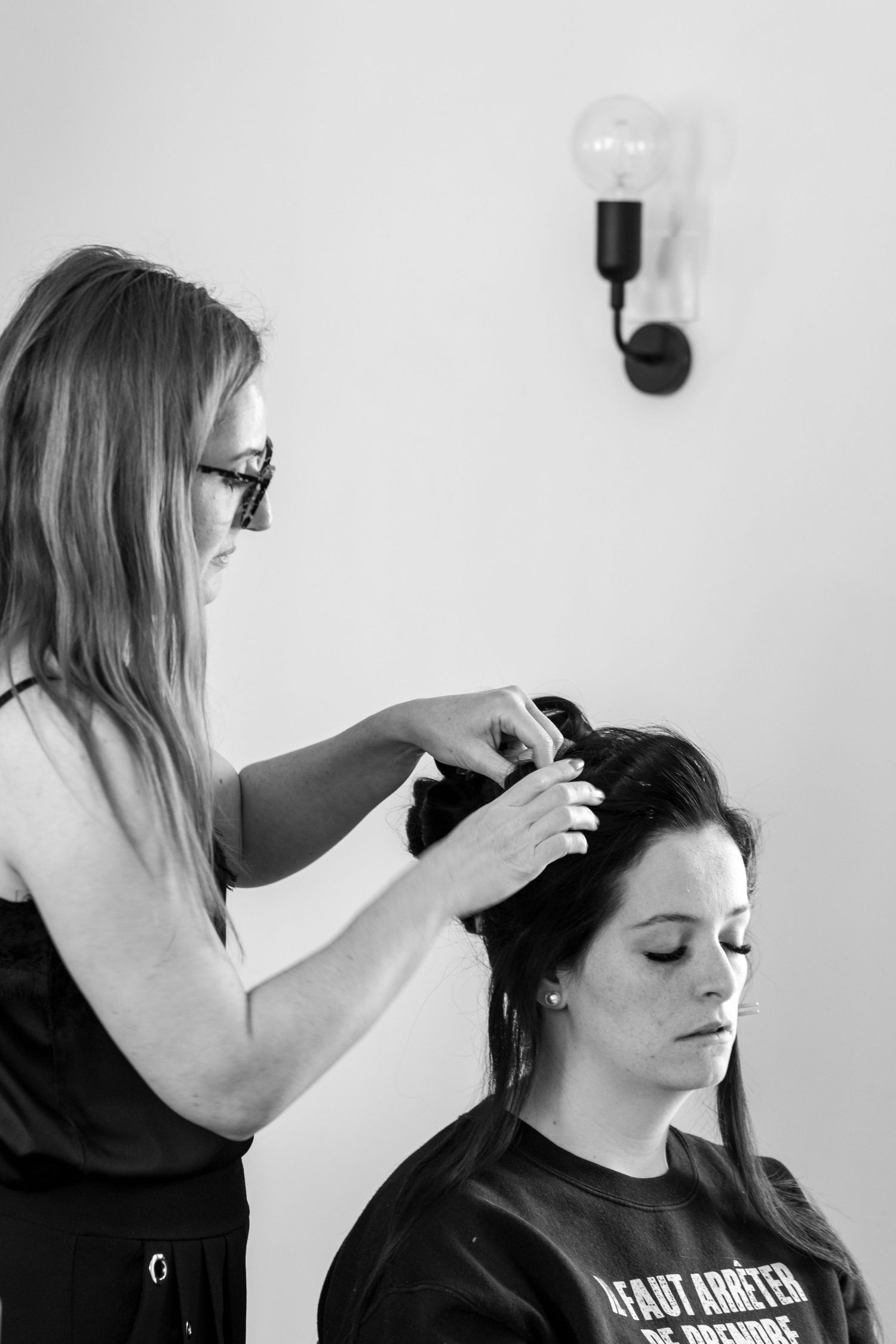 Black and white photo of a hairstylist styling a brunette woman's hair in a bright salon.