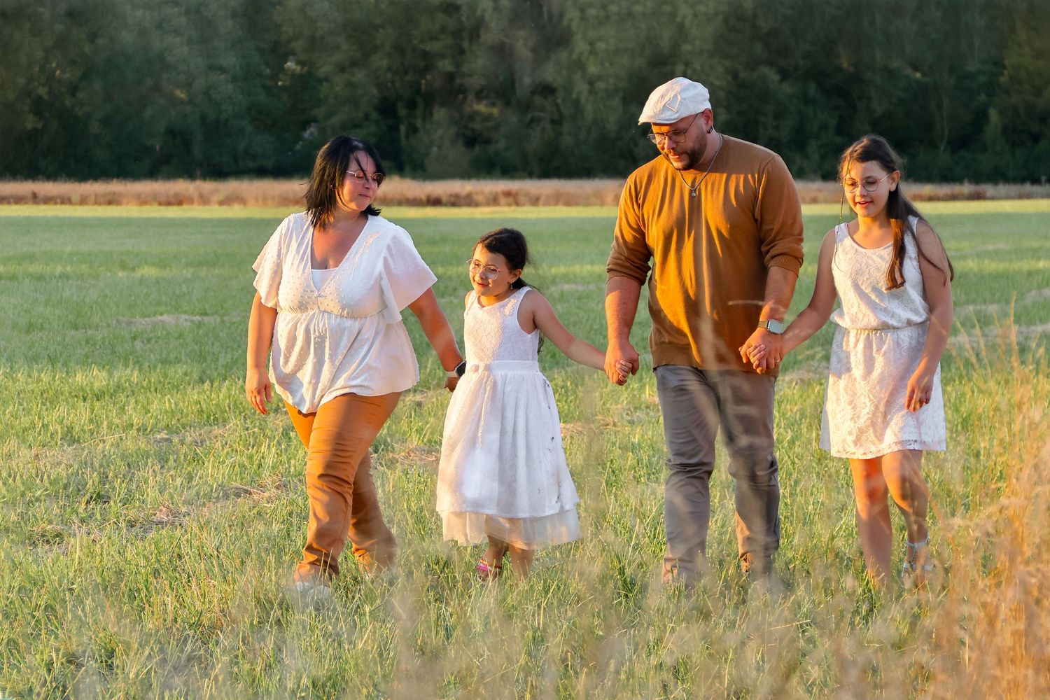 A happy family of four walking together through a sunlit green field.