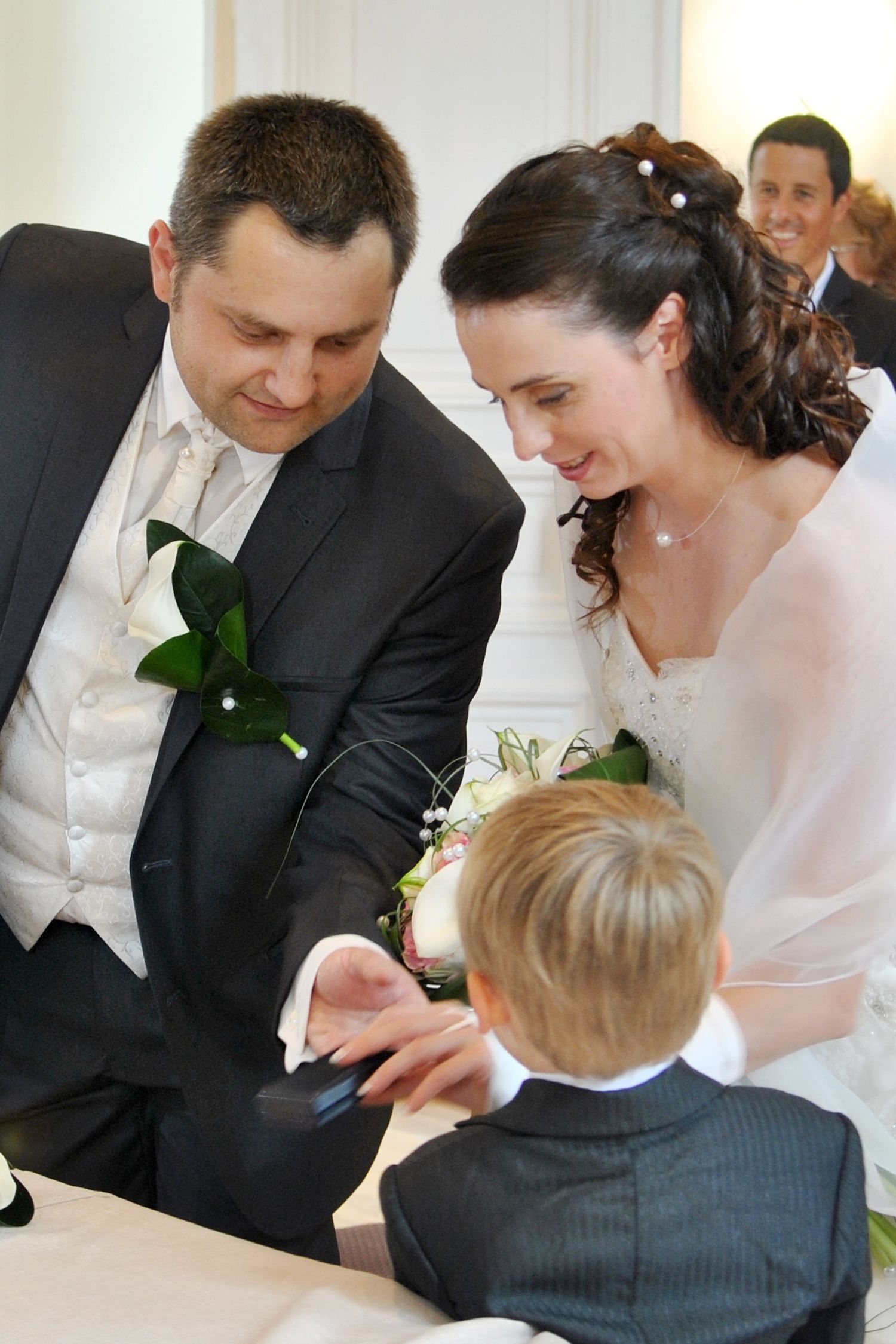 Bride and groom sharing a tender moment with young ring bearer at wedding ceremony.