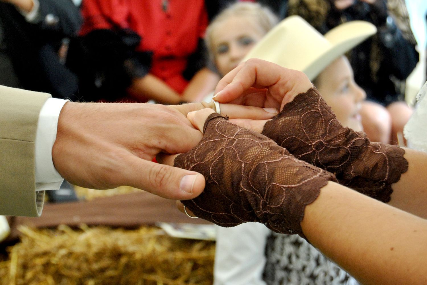 Groom places a wedding ring on the bride's hand adorned with brown lace gloves during a western-themed ceremony.