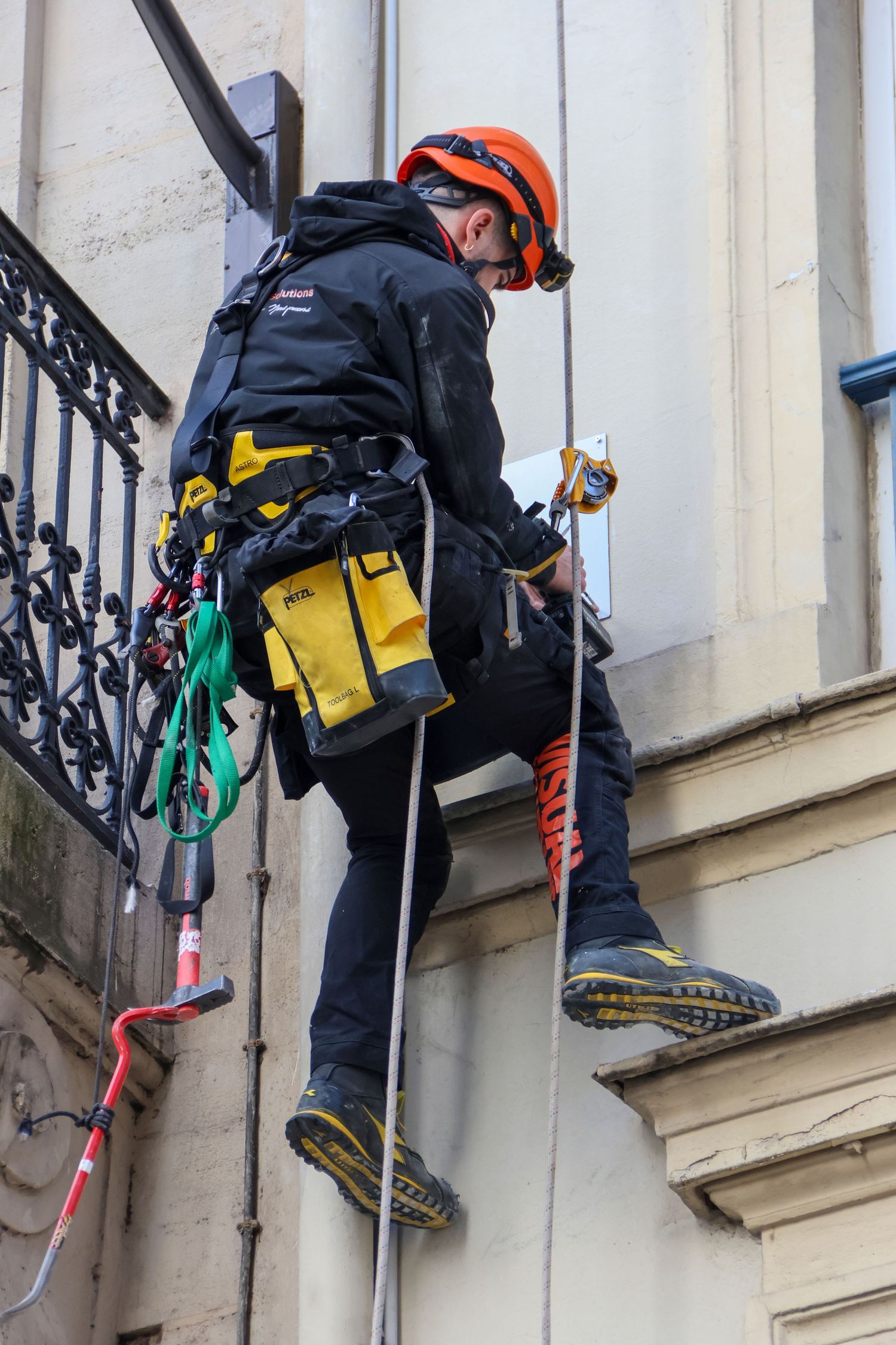 Industrial rope access worker in safety gear rappelling down a building facade during maintenance inspection.