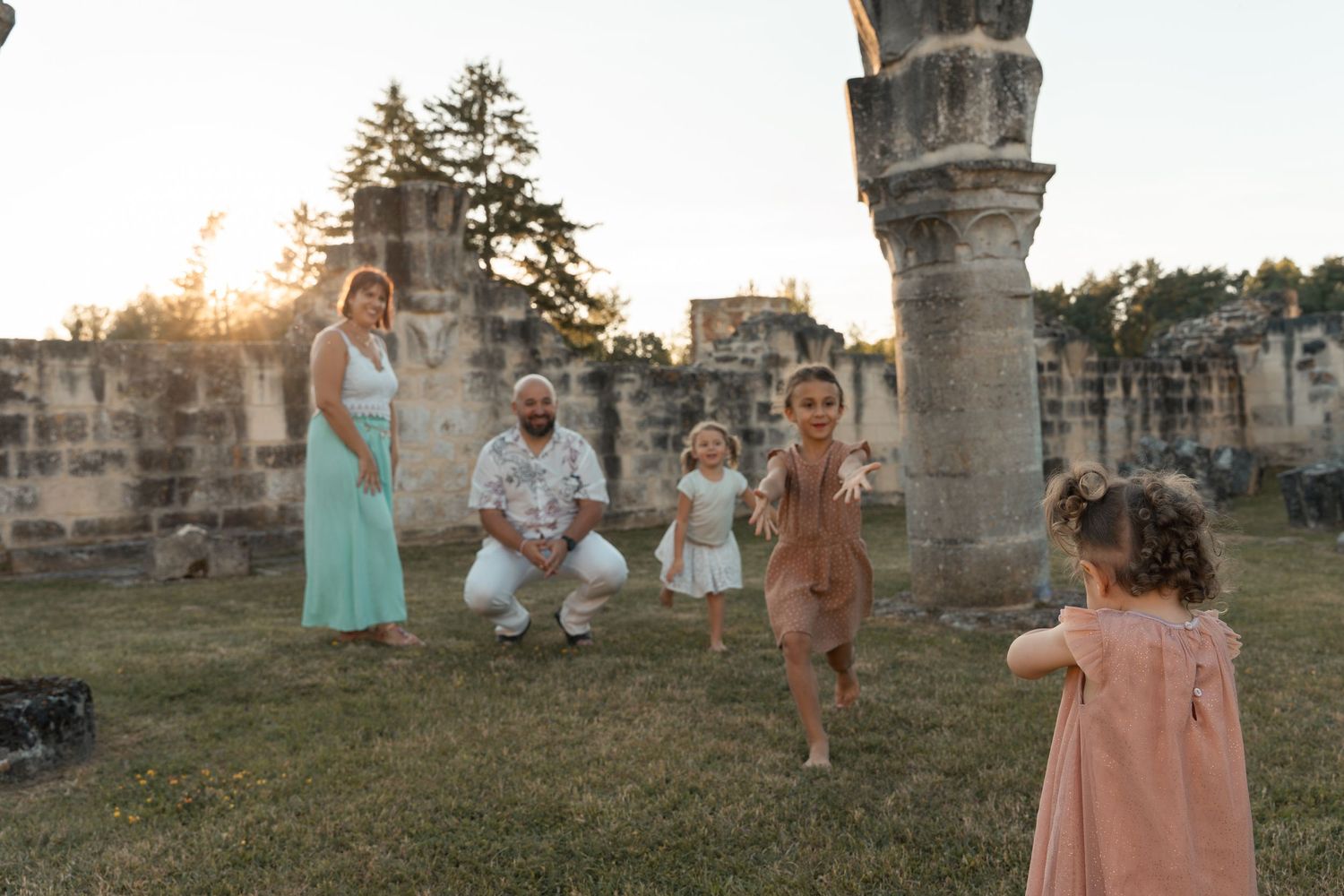 Family posing at sunset among ancient stone ruins, with two young children playing in a grassy outdoor setting.