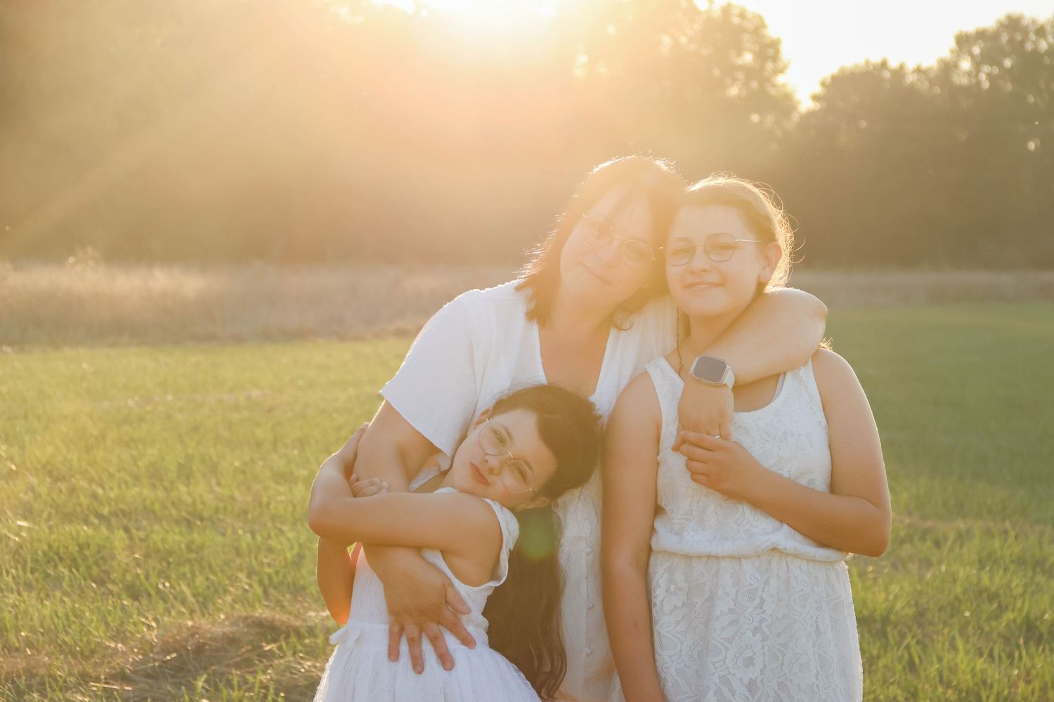 Séance famille lifestyle — maman serrant chaleureusement ses deux filles dans un magnifique champ doré au soleil couchant photographe Rethel