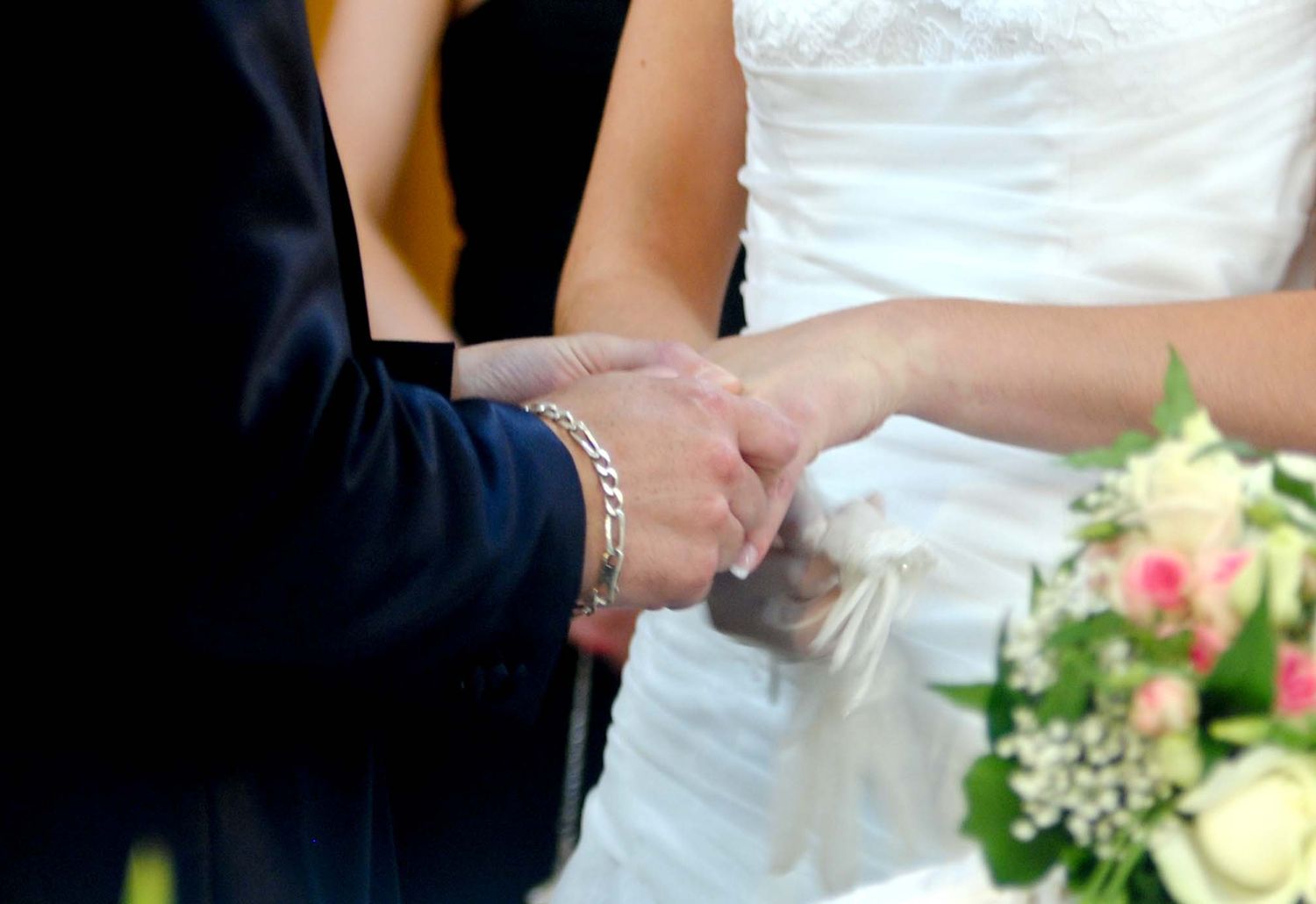A bride and groom holding hands during a wedding ceremony with a floral bouquet nearby.