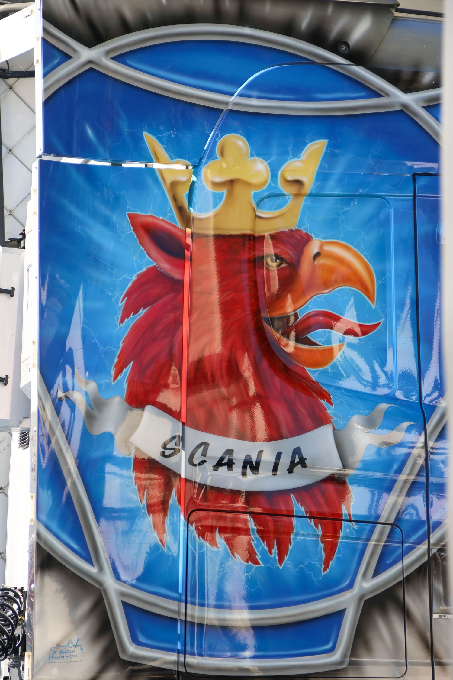 Colorful airbrushed Scania griffin logo artwork on a truck trailer panel with crown and banner design.