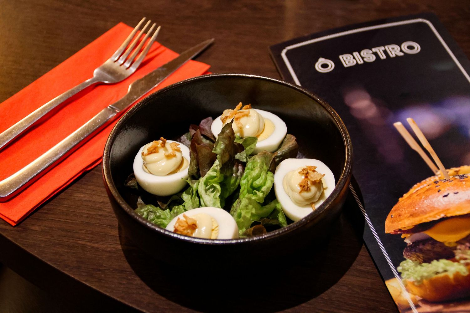 A fresh green salad bowl topped with halved boiled eggs and walnuts next to an O Bistro menu card.