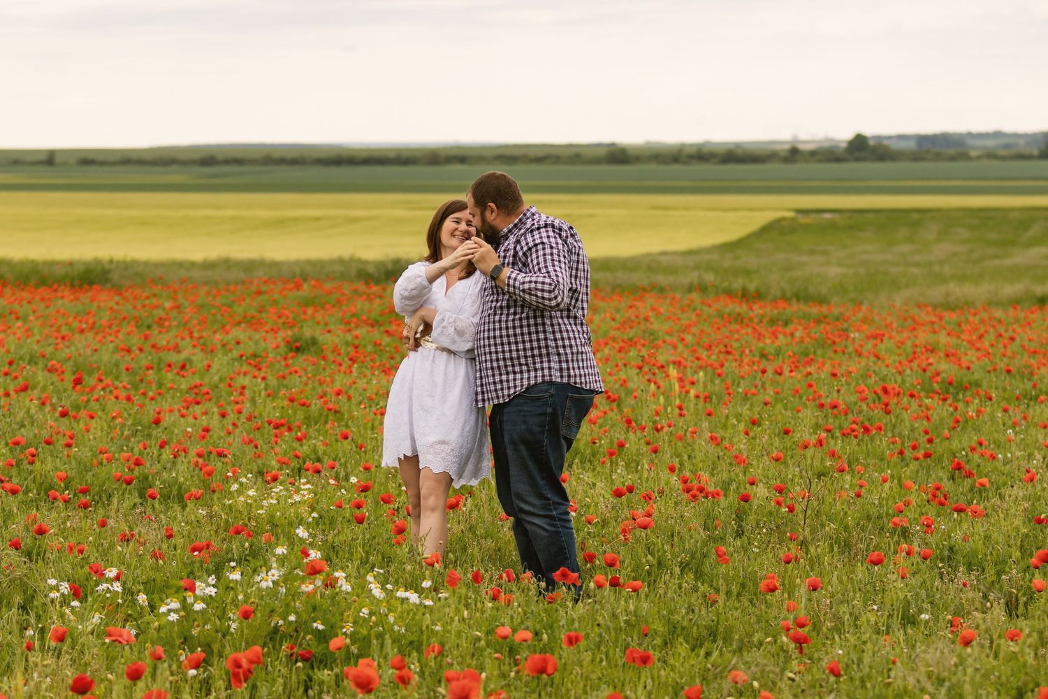 Couple dancing romantically in a vibrant red poppy field with green meadows in the background.