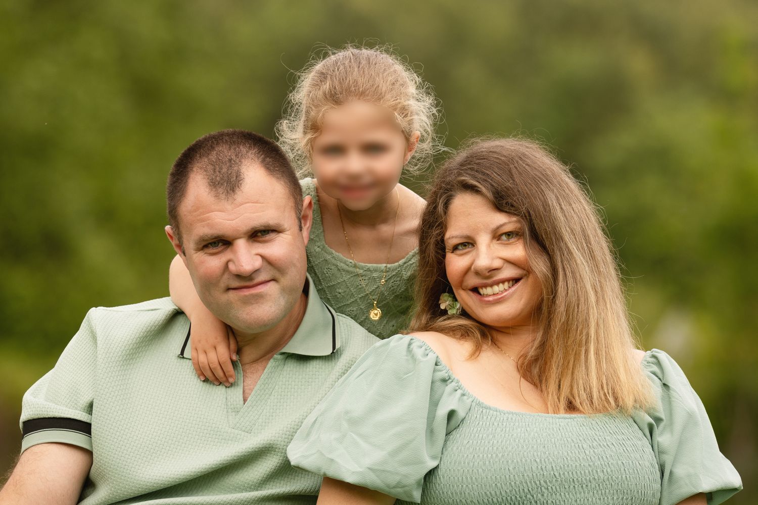 Happy family portrait of parents and young daughter outdoors with green nature background.