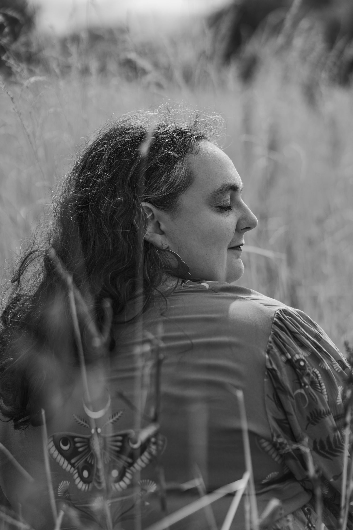 Black and white artistic portrait of woman with curly hair in field grass.