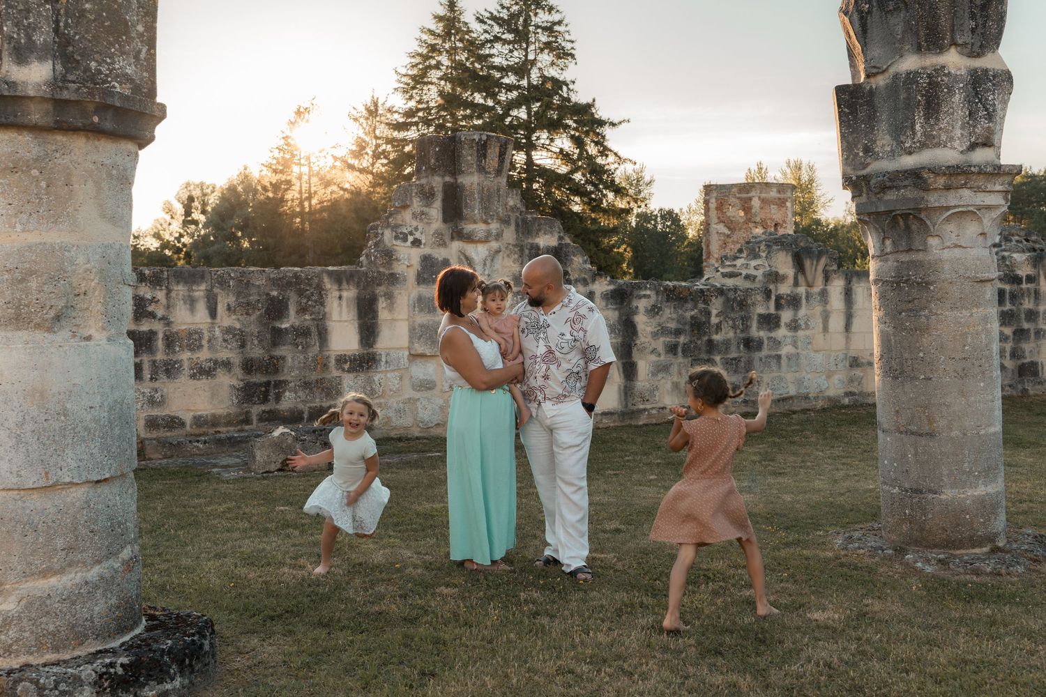 A joyful family dances and embraces among ancient stone ruins at golden hour, with two young children playing.