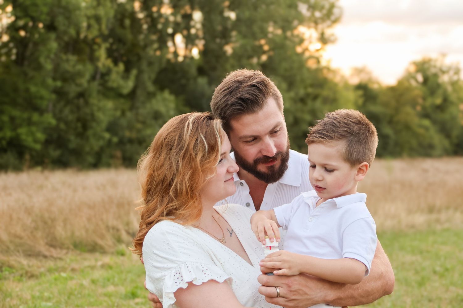 A happy family with a young boy enjoying a golden hour outdoor photo session in a green field.