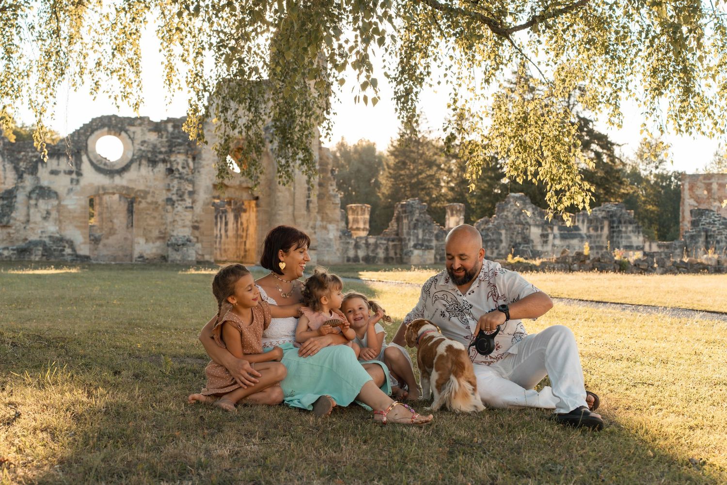 Happy family relaxing together on grass near ancient stone ruins during golden hour sunset outdoors.