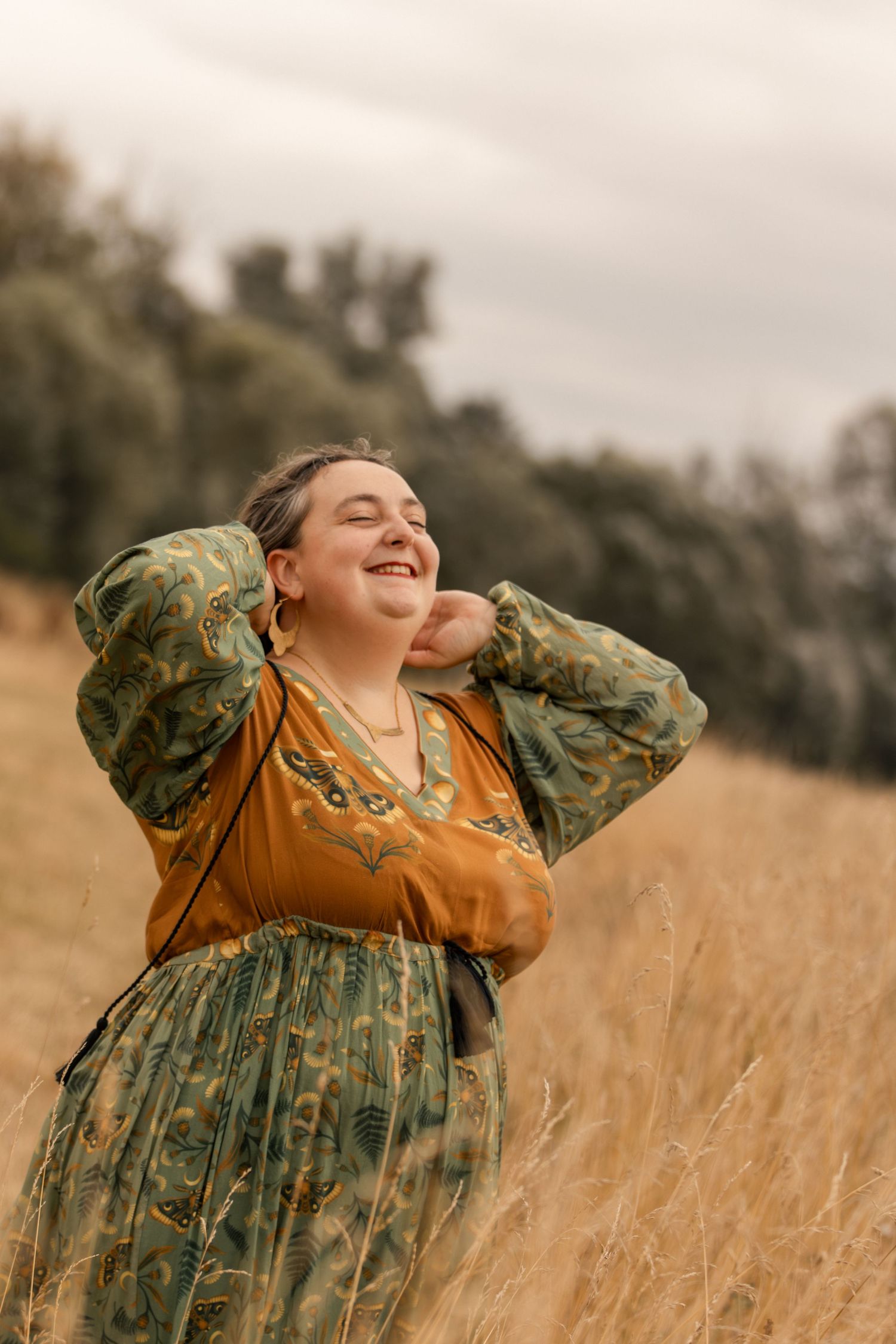 Joyful woman in floral green and mustard dress laughing in golden field.