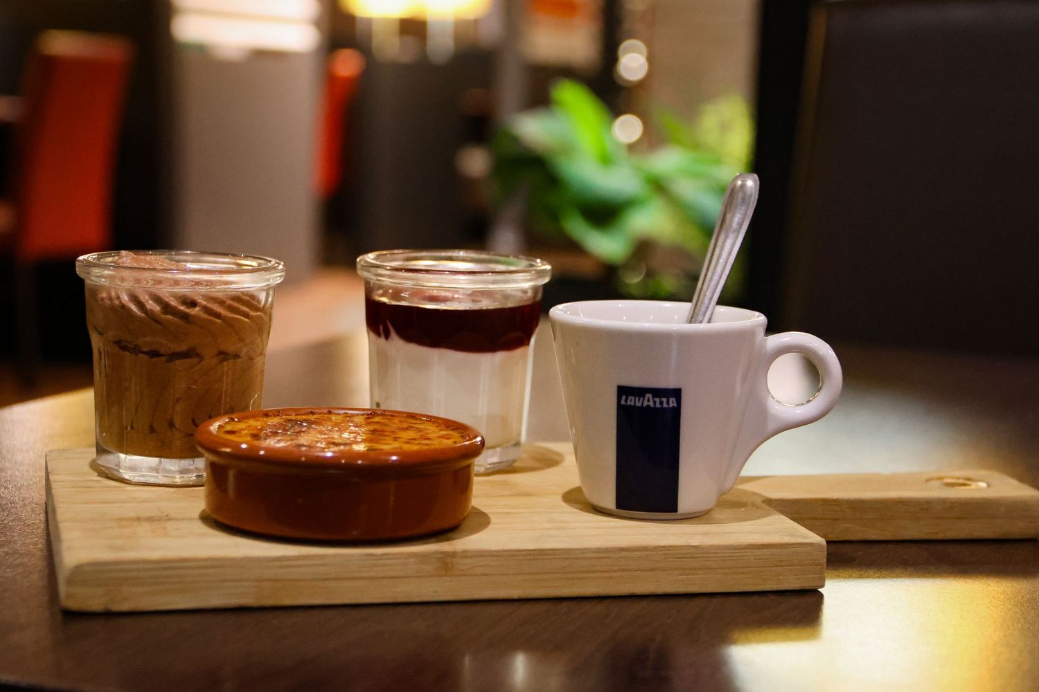 Coffee service set on a wooden board with espresso cups, a small dessert, and layered drinks.