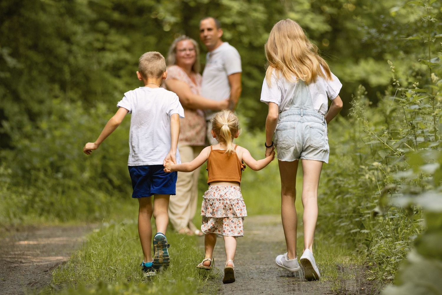 Family walking together on a scenic forest path, with children holding hands on a sunny summer day.