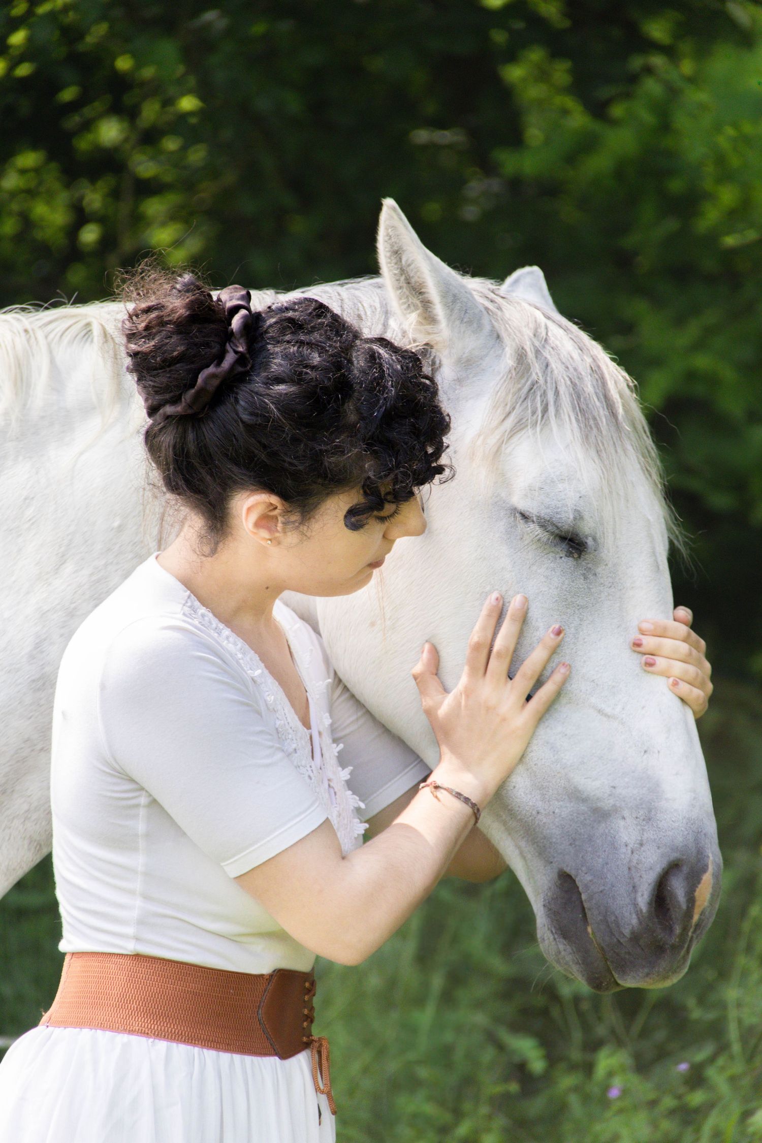 Séance cheval lifestyle — femme en robe blanche enlaçant tendrement son cheval blanc dans un cadre verdoyant, photographe Charleville