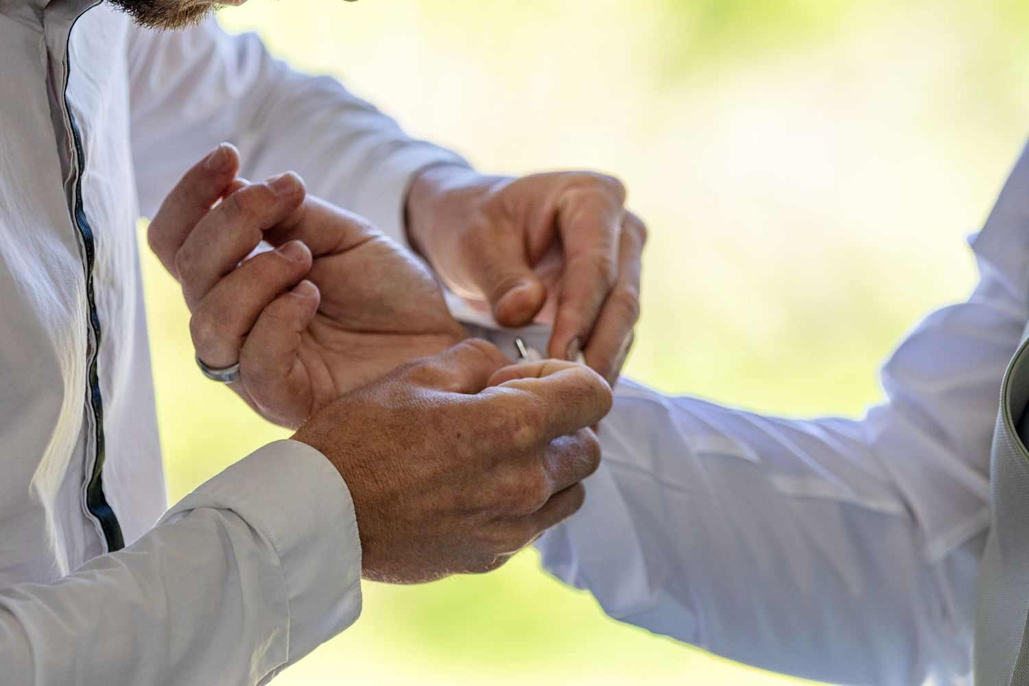 Two men in white shirts exchanging wedding rings during an outdoor ceremony.