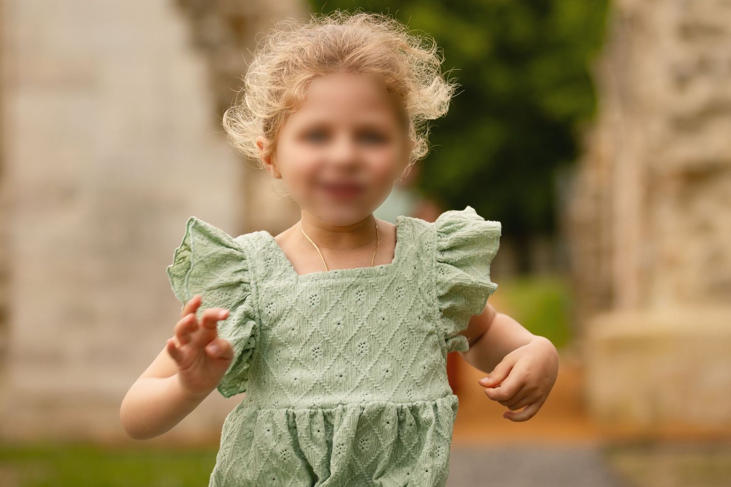 Young toddler girl in green eyelet dress playing outdoors with blurred background.