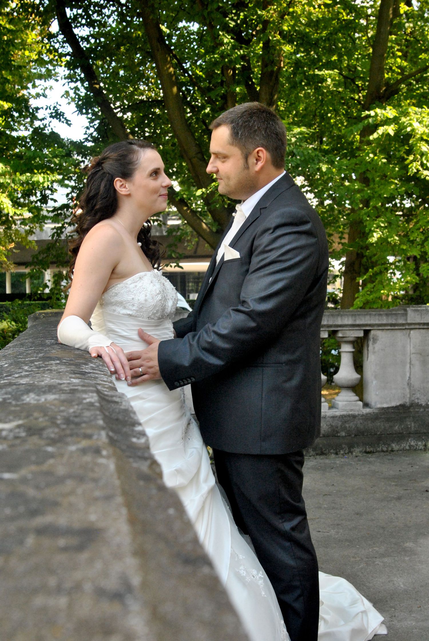 Bride and groom share a romantic moment outdoors, with the bride in a white strapless gown and groom in a gray suit.