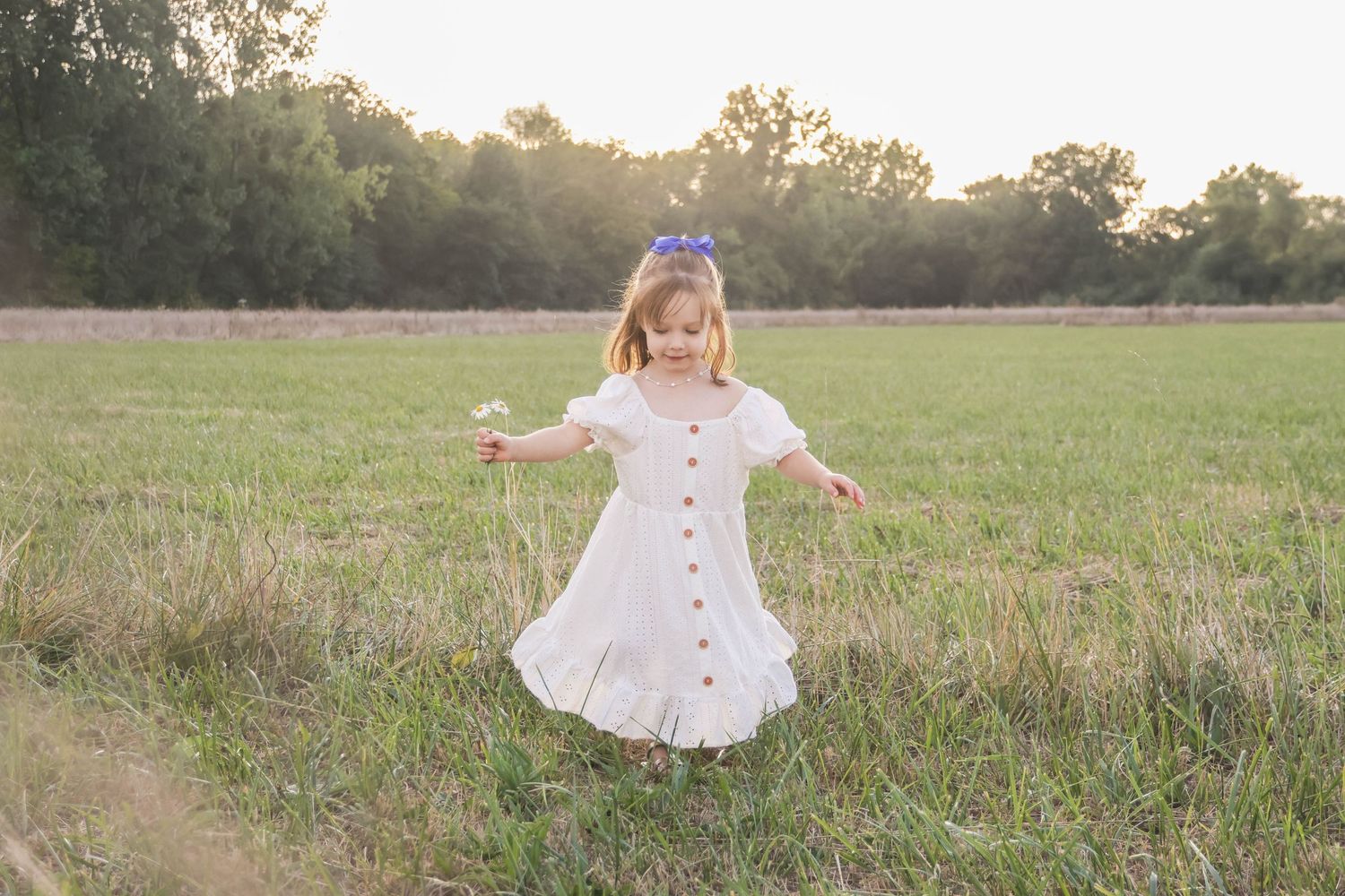 Séance famille lifestyle — petite fille en robe blanche virevoltant joyeusement dans un champ inondé de soleil, photographe Épernay Marne.