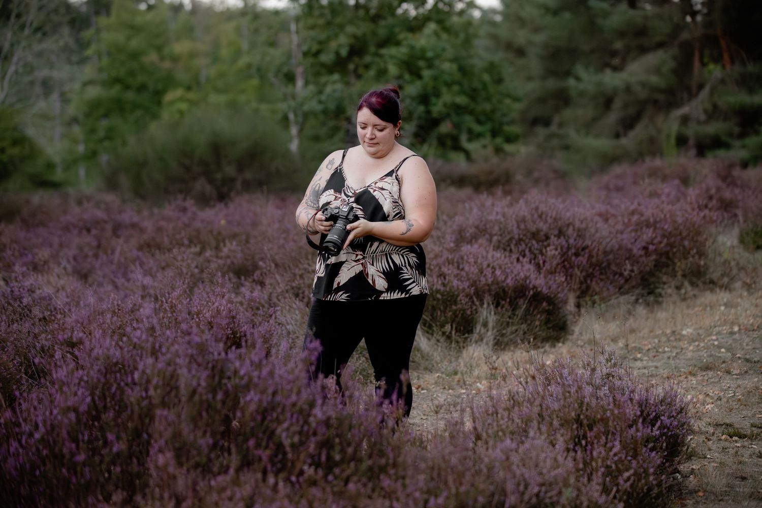 A red-haired woman looks down at a small dog she is holding in a purple heather field.