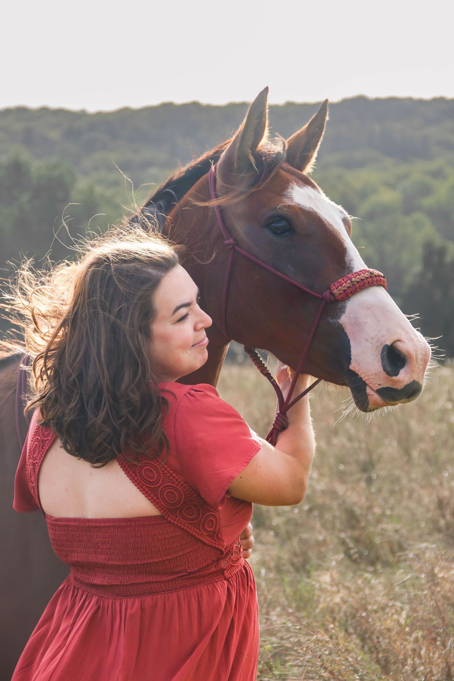 Séance cheval lifestyle — femme en robe rouge nez à nez avec son cheval alezan dans un champ, photographe Épernay Marne.