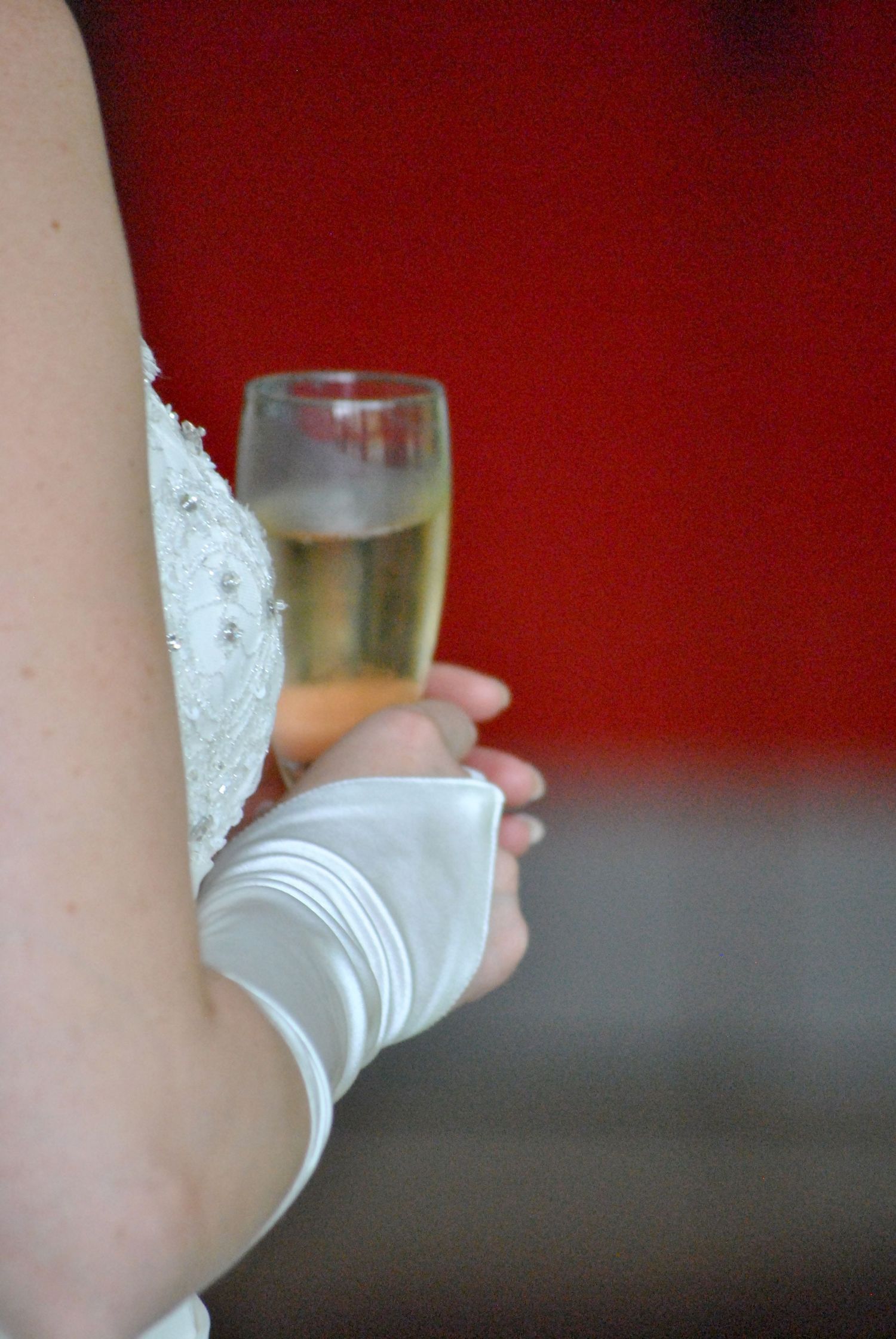 Bride in white lace gown and gloves holding champagne flute at wedding reception.