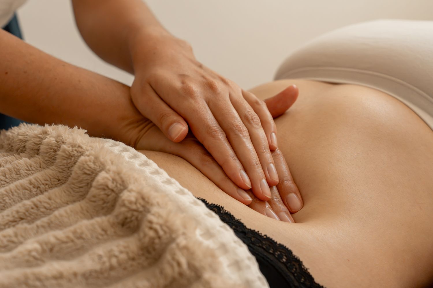 Therapist performing abdominal massage therapy on a client lying on a treatment table in a spa setting.