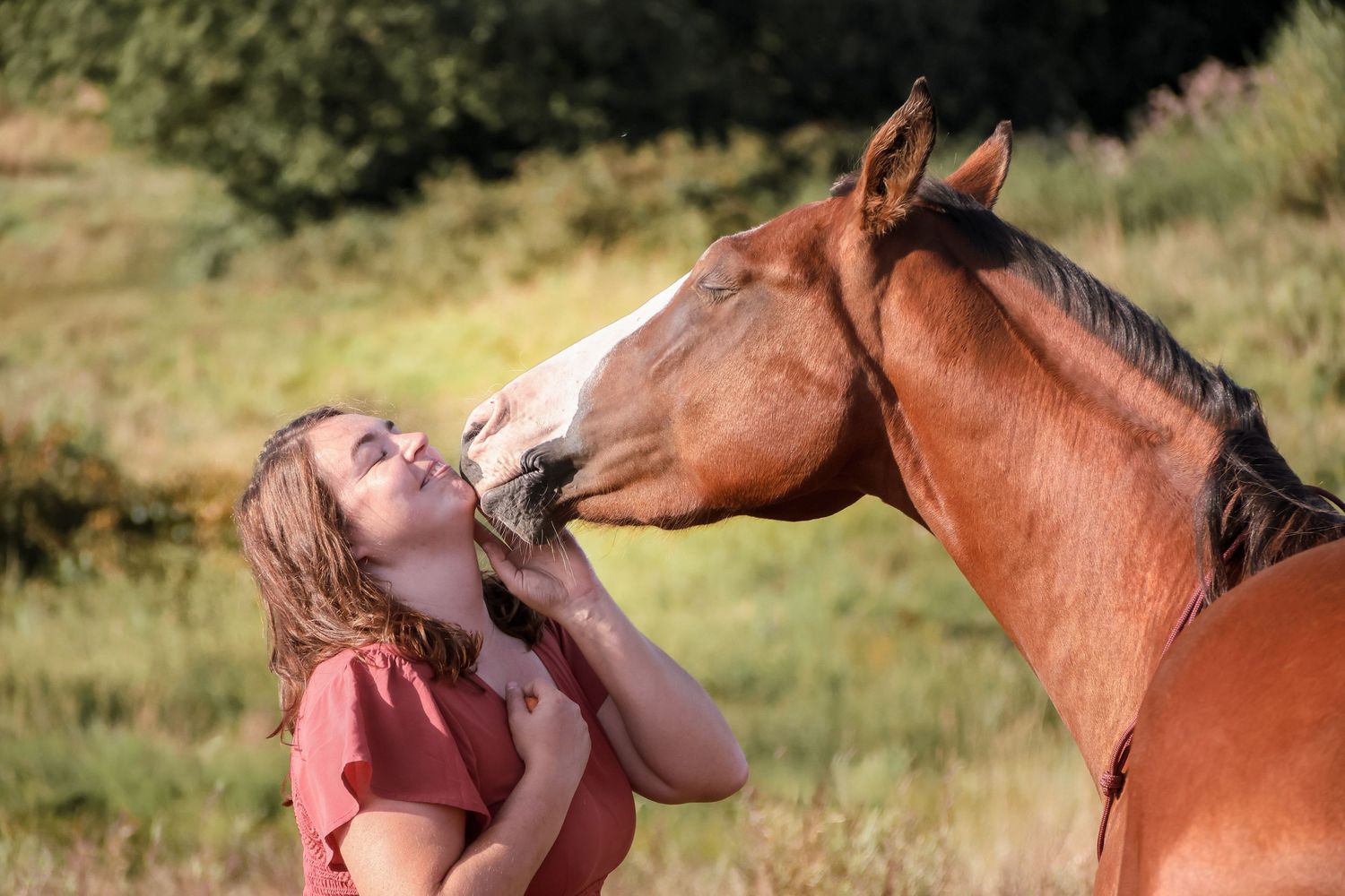 Girl in pink top sharing a kiss with a chestnut horse outdoors.