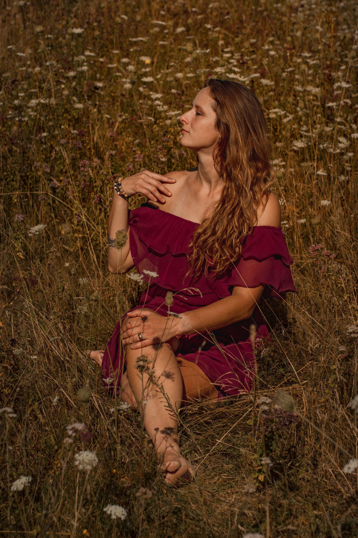 Woman in red off-shoulder dress sitting gracefully in a wildflower field, golden hour light enhancing her bohemian style.