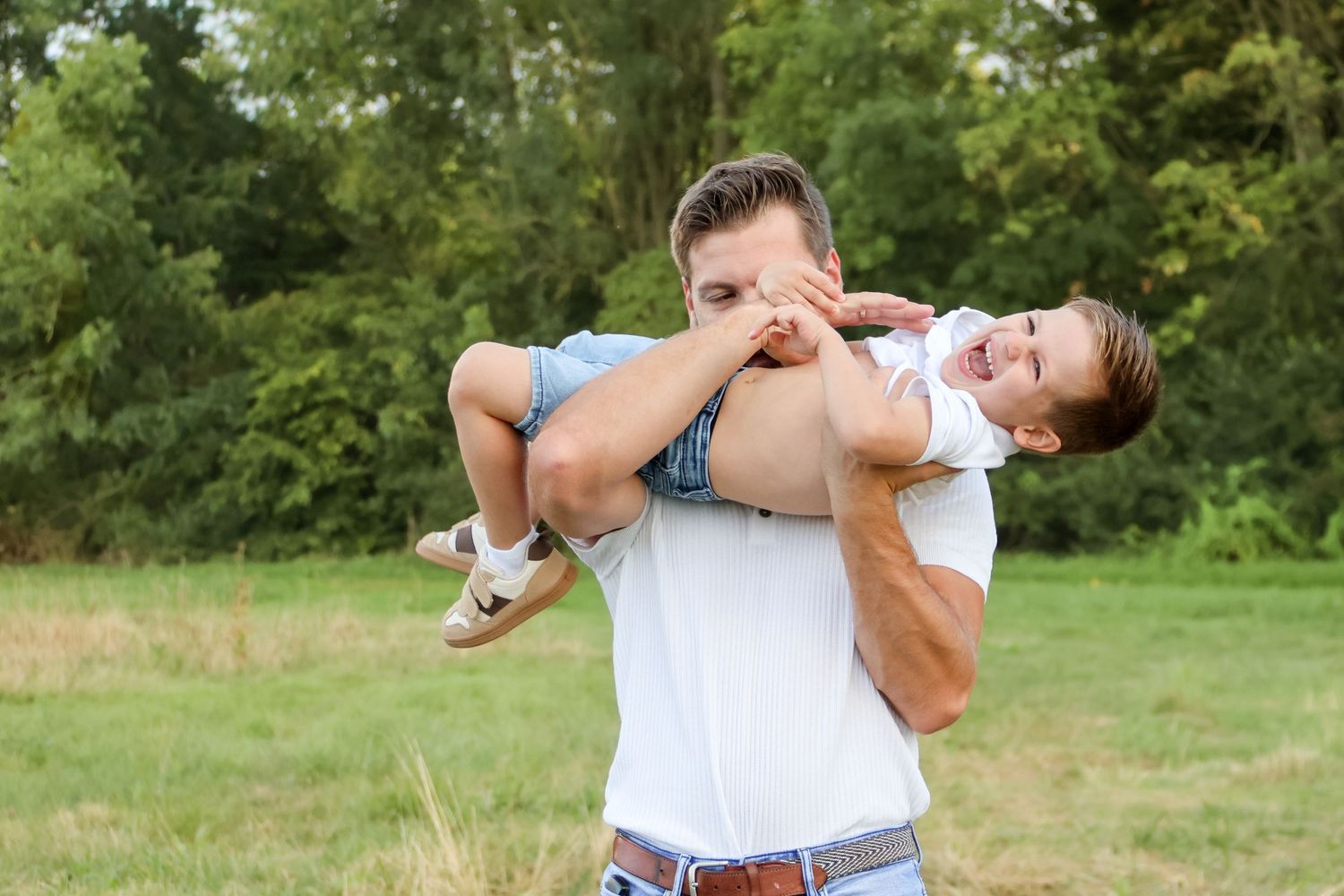 Father lifting his happy toddler high in the air during outdoor family playtime in a grassy field.