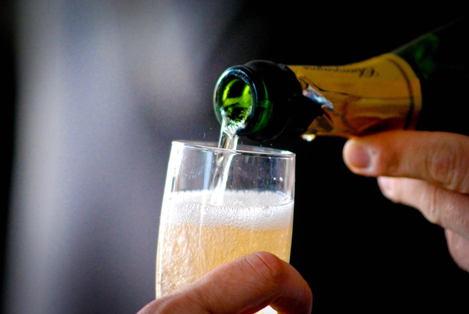 Champagne being poured from a green bottle into a crystal flute glass, creating bubbles and froth.
