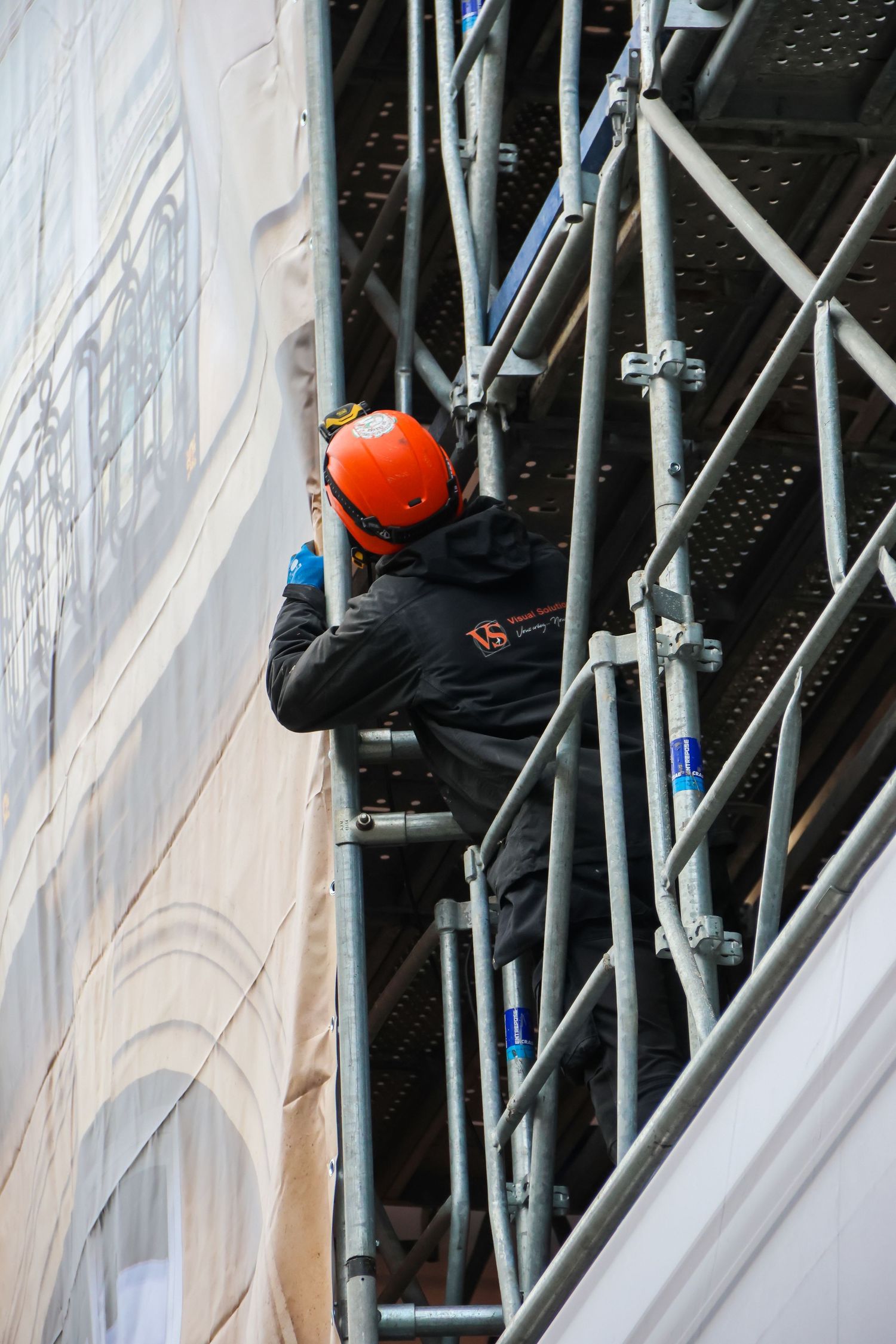 Construction worker in orange helmet on scaffolding painting a building facade.