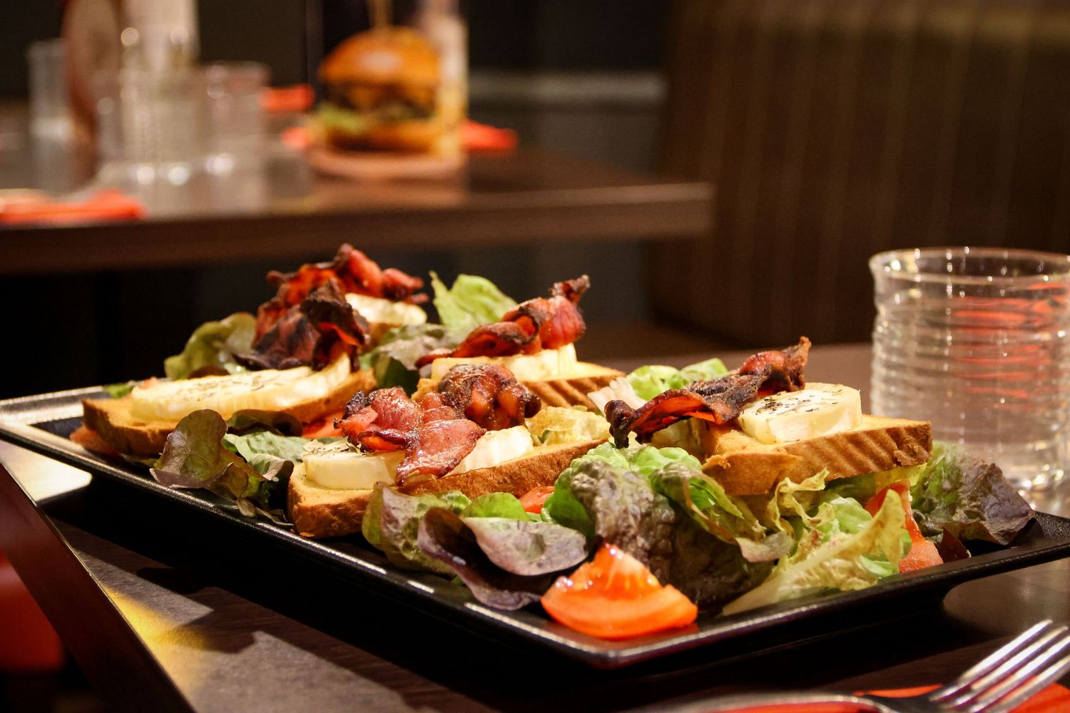 A gourmet salad plate with bacon, croutons, lettuce, and mixed toppings on a dark platter in a restaurant setting.