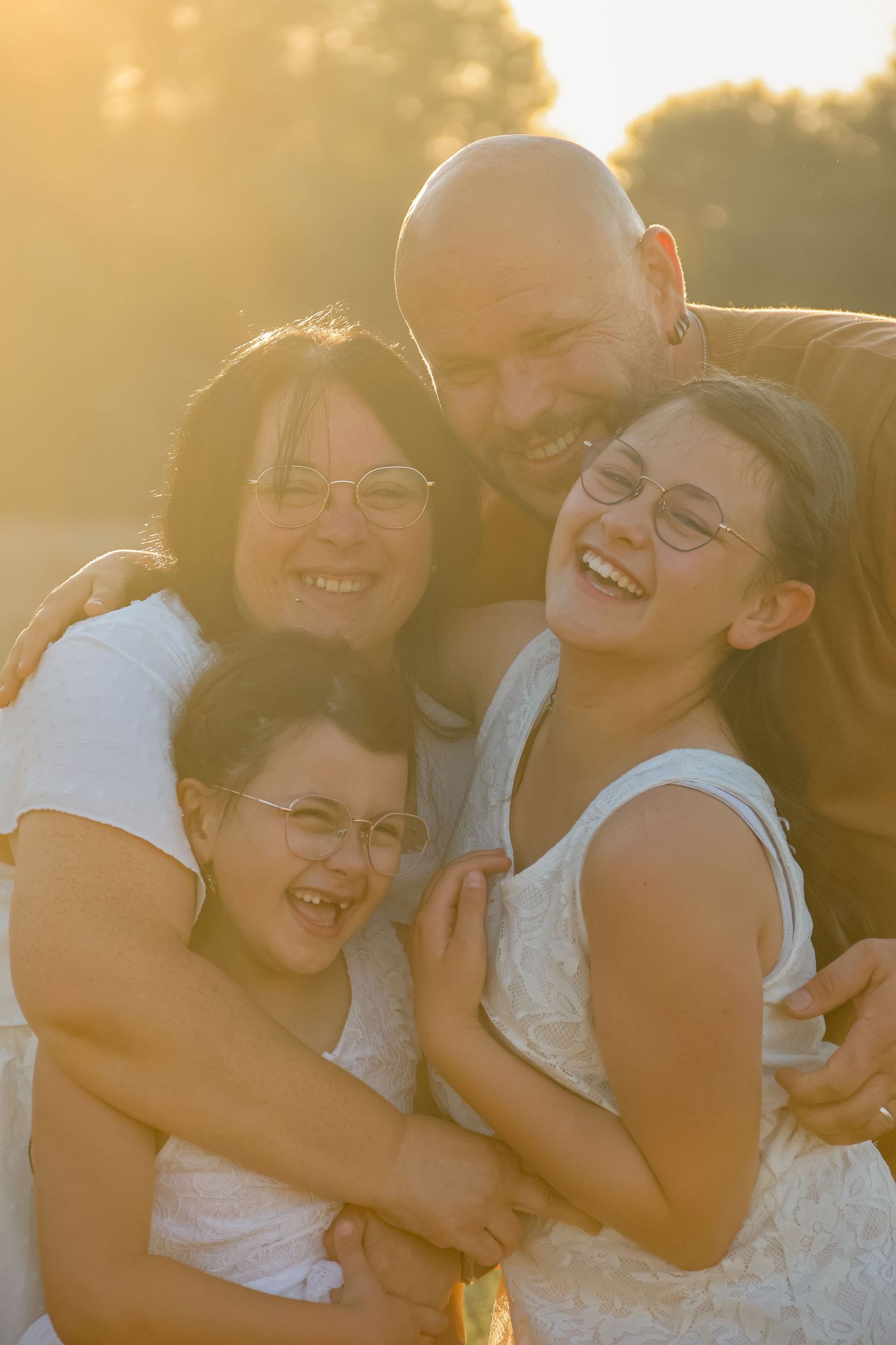 A happy family of four laughs together outdoors in warm golden sunset light.