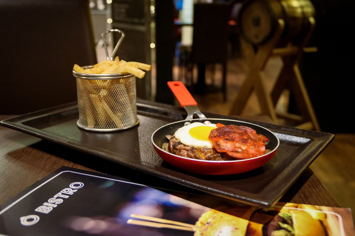 Red skillet with fried egg and meat patty served on a tray with crispy fries in a basket at O Bistro restaurant.