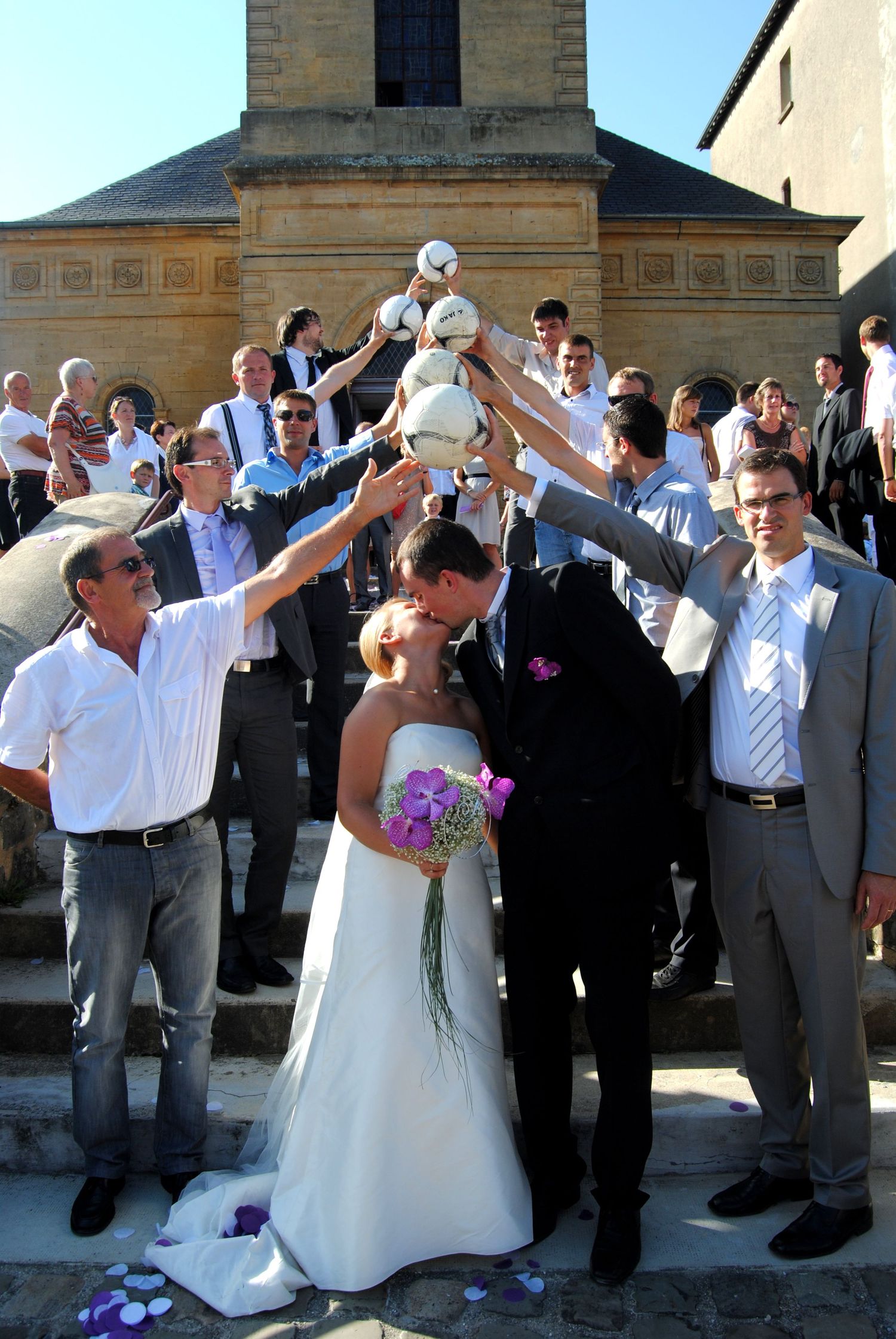 Wedding couple kissing on church steps surrounded by guests raising white doves in celebration.
