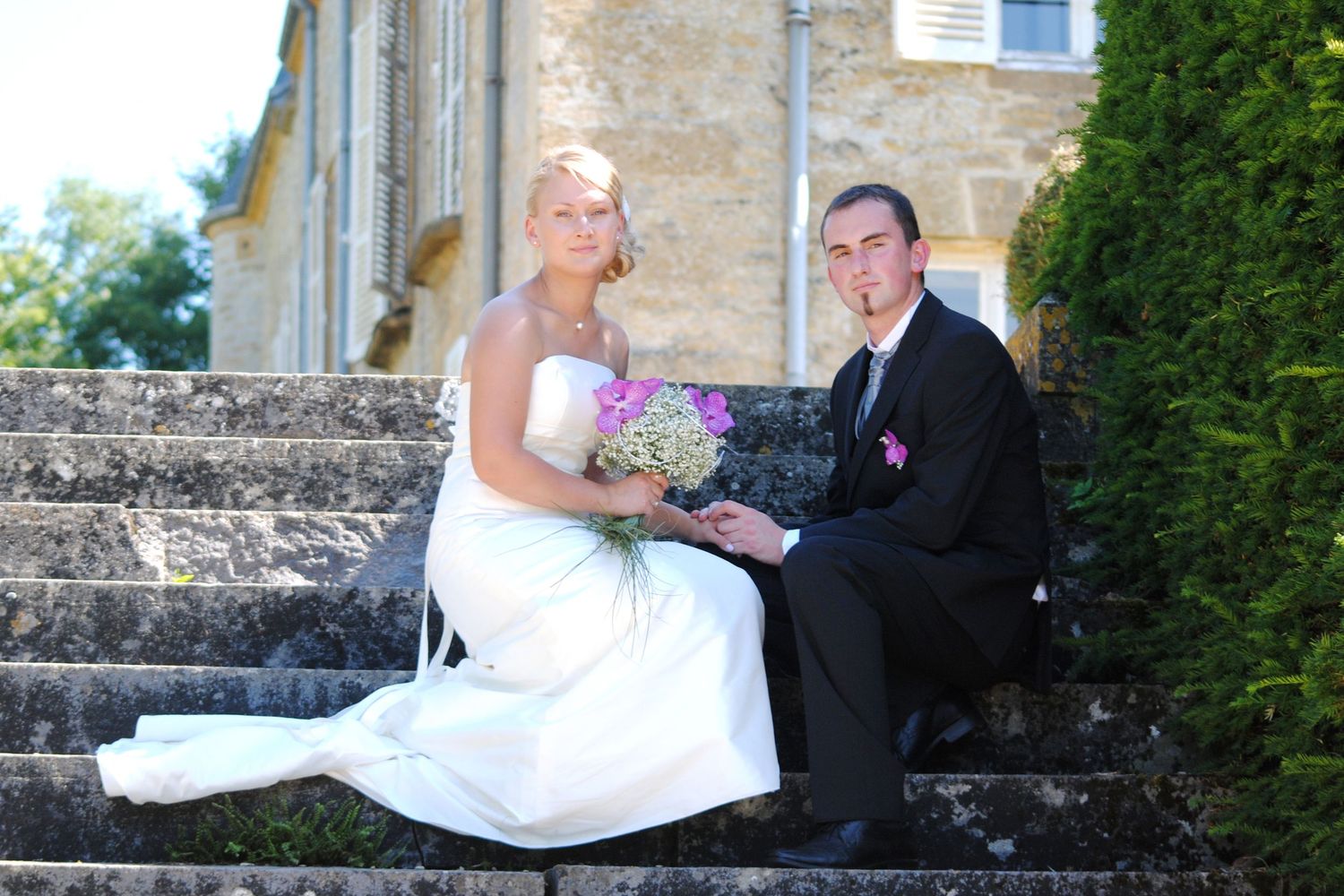Bride and groom sitting on stone steps outside a historic building on their wedding day.