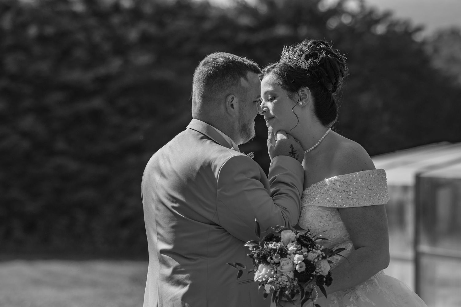 Black and white wedding photo of bride and groom sharing an intimate moment, bride holding a bouquet outdoors.